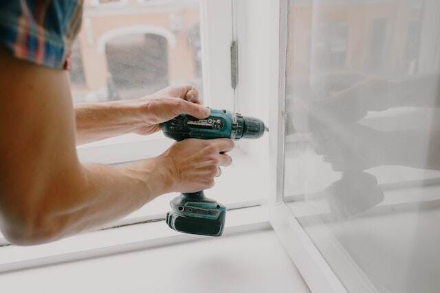 person using an electric drill to fix the hinge of a window